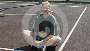 Tired Happy female basketball player sitting with ball on court in open air, having rest