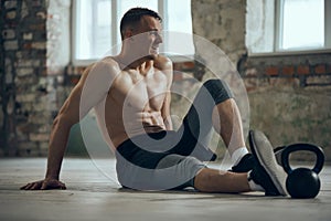 Tired after hard training session. Young muscular man sitting on floor shirtless with sweating body. Concept of sportive