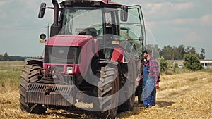 Tired hardworking farmer in overalls near a modern energy-saturated tractor