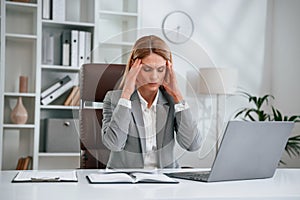 Tired, having headache. Woman in business formal clothes is working in office