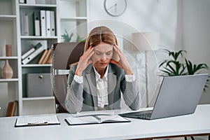 Tired, having headache. Woman in business formal clothes is working in office