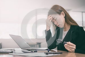 Tired and headache asian business woman closed eyes and holding glasses sitting at desk in front of laptop at office background