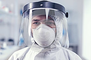 Tired healthcare scientist loooking at camera wearing ppe suit with face shield photo