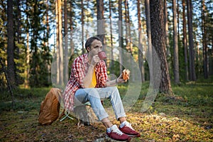 Tired hiker camper man eating sandwich drinking tea on break halt in forest enjoying nature.