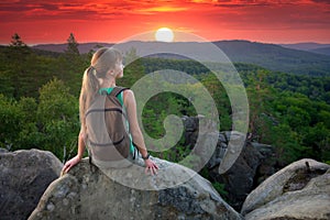 Tired hiker girl relaxing on rocky mountain top enjoying evening nature during travelling on wilderness trail. Lonely