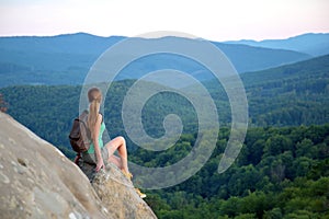 Tired hiker girl relaxing on rocky mountain top enjoying evening nature during travelling on wilderness trail. Lonely