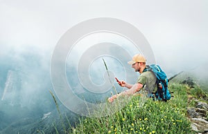 Tired hiker man with backpack browsing internet using smartphone enjoying cloudy valley bottom walking by the foggy cloudy weather