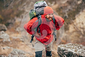 Tired hiker man hiking in mountains dressed in red clothes exploring new places. Traveler bearded male trekking and mountaineering