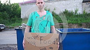 Tired hobo man on the street. Sign on cardboard - will work for food