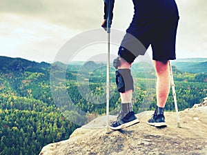 Tired hurt tourist with medicine crutches. Man with broken leg in knee brace features resting on exposed rocky summit