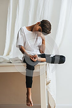 Tired indian asian kid sitting on a table, holding his foot