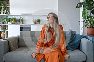 Tired indifferent blonde middle aged woman sit sofa thoughtfully look aside need relaxation at home.