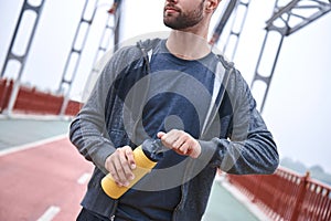 Tired after jogging. Young manin sports clothing bending and looking tired while standing on the bridge and urban view