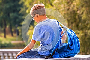 Tired kid with backpack sitting outdoors after school