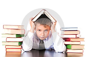 A tired, lagging schoolboy boy sits in a library with books and learns lessons. Unwillingness to learn