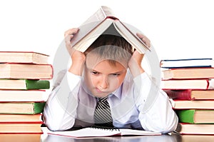 A tired, lagging schoolboy boy sits in a library with books and learns lessons. Unwillingness to learn