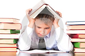 A tired, lagging schoolboy boy sits in a library with books and learns lessons. Unwillingness to learn