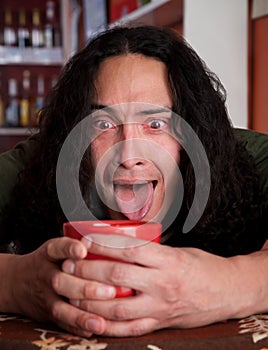 Tired Latino man cradling red coffee cup