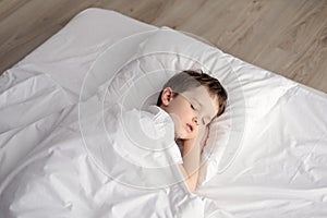 Tired little boy sleeping in bed, happy bedtime in white bedroom