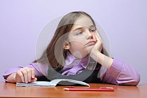 Tired little school girl doing homeworks at desk