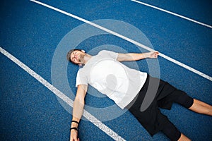 Tired male athlete resting after running while lying on racetrack