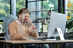 Tired male freelancer, programmer rubs his eyes, suffers from overfatigue, discomfort long sitting work in home office