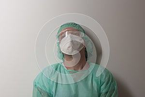 Tired male nurse, with plastic protective eyeglasses and respirator ffp2, cap, gown, with  personal protective equipment to