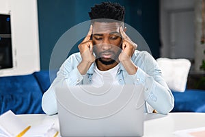 Tired male office employee holding hands at his head while looking at the laptop screen, feeling boring and angry. Bored