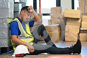 Tired male warehouse worker sitting on floor and taking break from hard work in large retail warehouse