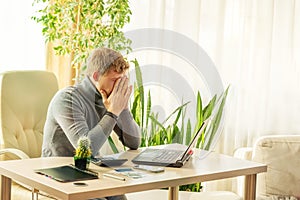 Tired man covering his face with his hands at the workplace at the table