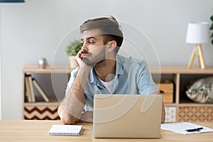 Tired man distracted from computer work lacking motivation