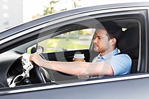 Tired man driving car with takeaway coffee