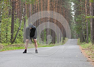 Tired man in grey hoodie making a stop after jogging on road in the forest, selective focus