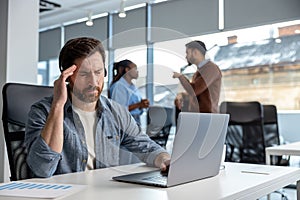 Tired man in headset working on laptop in coworking environment