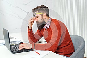 Tired man with laptop computer at working place. Bearded man overworked at office. Stressed handsome business man. Feeling photo