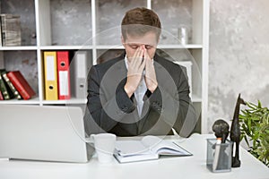 Tired man manager with laptop and planner feeling exhausted at his working place in office with hands near his face looking