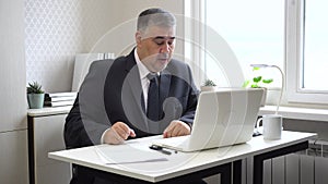 A tired man in an office setting yawns and rubs his eyes due to computer strain