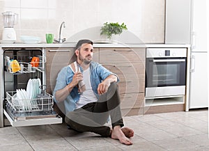 Tired man beside open dishwasher