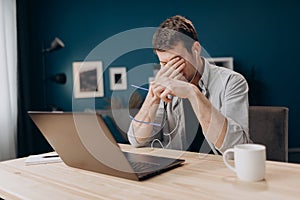 Tired man rubbing eyes after long working day with laptop