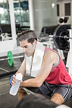 Tired man sitting on bench holding bottle of water