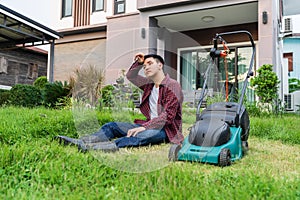 Tired man sitting with law mower for cutting grass at home