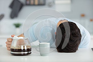 tired man sittingwith jug coffee and sleeping