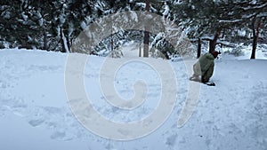 Tired man with snow skate sitting on snowboard on snow in wild woods. Fun leisure time in the forest snowboarding