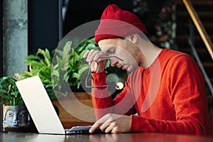 Tired man taking a break during online work on laptop, holding head in hand, feeling lack of energy.