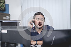 A tired man talks to someone over the phone while sitting at his desk during extended overtime at the office