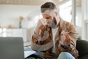 Tired Man Touching Nosebridge Sitting At Laptop Holding Eyeglasses Indoor