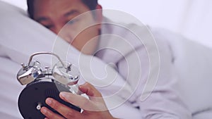 Tired Man waking up to alarm clock and looking at the time stressfully