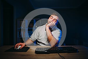 A tired man in a white T-shirt fell asleep while working at home on the computer at night