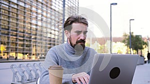 Tired man working stressed on his laptop in a coffee shop terrace, serious and frustrated for his bad investments.