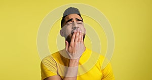 Tired man yawning over yellow background